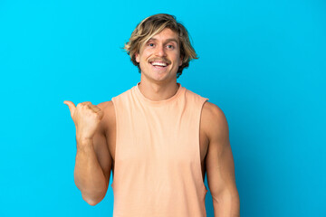 Handsome blonde man isolated on blue background pointing to the side to present a product
