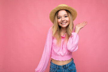 Young beautiful woman in stylish pink summer blouse and trendy straw hat. Positive female shows facial emotions. Funny model isolated on pink background with free space