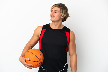 Young blonde man holding a ball of basketball isolated on white background looking to the side and smiling