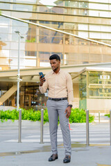 Fototapeta na wymiar Full length portrait of young handsome African businessman in city using mobile phone