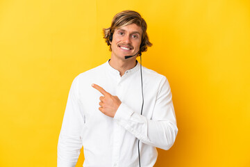 Telemarketer man working with a headset isolated on yellow background pointing to the side to present a product