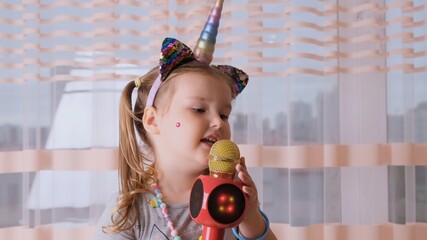 funny cute little girl 4-5 years old, singing into a karaoke microphone, with a unicorn headband, child singing karaoke music, have fun at an event future musician loud voice solo