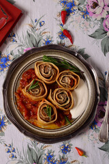 Egg dough rolls with minced meat with sour cream, butter and tomato sauce on a plate. On a linen tablecloth.
