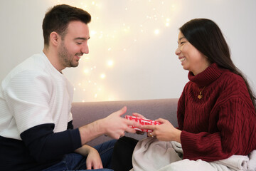 Young asian woman giving a Christmas present to his caucasian boyfriend.