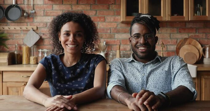 Attractive African couple sit in kitchen at home smile look at camera wave hands make video call talking to family remotely use video conferencing application. Virtual meeting, communication concept