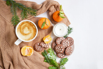 Big cup of coffee with milk, clementine and chocolate cookies on the white bedsheet. Fir tree branches around coffee and dessert. Christmas, new year mood composition. Holiday morning time. Template.