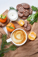 Big cup of coffee with milk, clementine and chocolate cookies on the white bedsheet. Fir tree branches around coffee and dessert. Christmas, new year mood composition. Holiday morning time. Top view. 