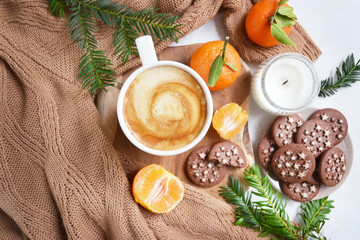 Obraz na płótnie Canvas Big cup of coffee with milk, clementine and chocolate cookies on the white bedsheet. Fir tree branches around coffee and dessert. Christmas, new year mood composition. Holiday morning time. Top view. 