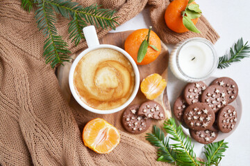 Big cup of coffee with milk, clementine and chocolate cookies on the white bedsheet. Fir tree branches around coffee and dessert. Christmas, new year mood composition. Holiday morning time. Top view. 