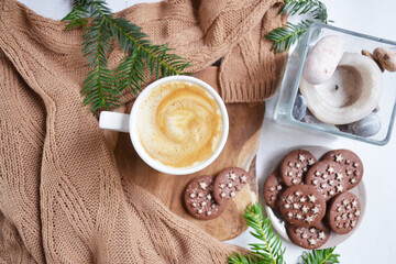 Big cup of coffee with milk and chocolate cookies on the white bedsheet. Fir tree branches around coffee and dessert. Christmas, new year mood composition. Holiday morning time. Top view. 
