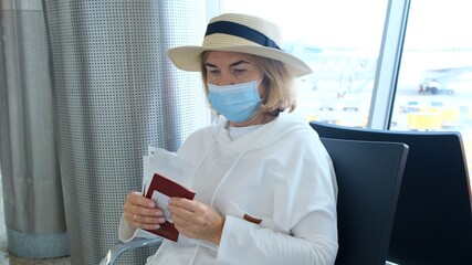 Female aged 50-55, wearing a hat and a protective mask, sits at the check in counters in the airport terminal due to travel restrictions due to the coronavirus. Covid-19 pandemic. Sanitary measures
