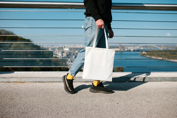 Cropped photo of a young man with a white fabric eco bag against an urban city. Eco friendly....