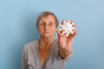 Senior woman is holding a coronovirus model on blue background. Person against coronovirus. Hand is holding model Coronavirus . Coronovirus molecule printed model on a 3D printer.