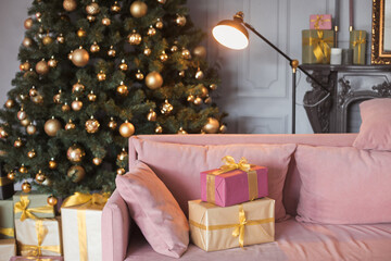Hall room fashion interior with a velvet couch, black modern fireplace and gorgeous decorated Christmas tree with many gift boxes in lounge with presents in gold, light green and pink color