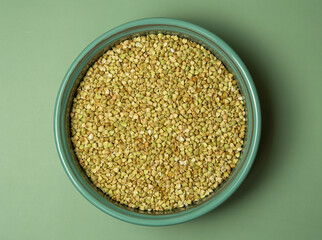 Peeled buckwheat seeds in wooden spoon isolated on green background
