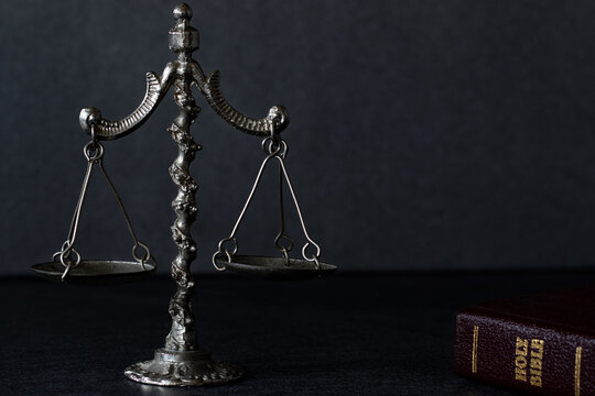 Vintage weighing balance scale on dark background with closed Holy Bible Book. Christian biblical concept of Law and justice. Old ancient rustic symbol of comparison and measure. A close-up.