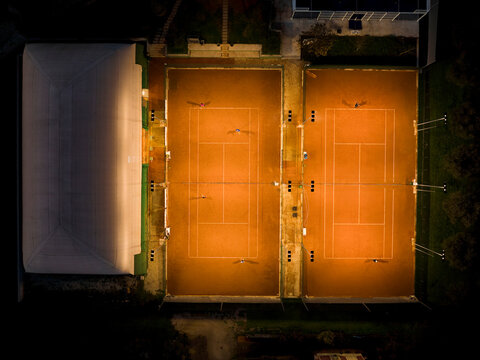 View from above, aerial view of some people playing tennis on a clay court at night.