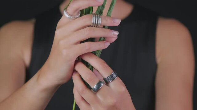 PAN close up of unrecognizable female model wearing designer metal rings holding flowers and posing isolated on black background