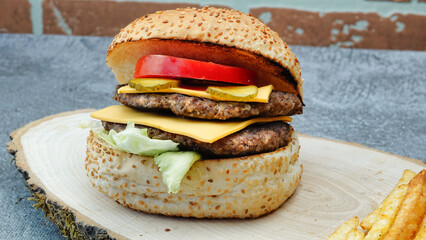 A juicy grilled double hamburger with lettuce, cheddar cheese, onions, tomato on wood board, front of red vintage brick wall