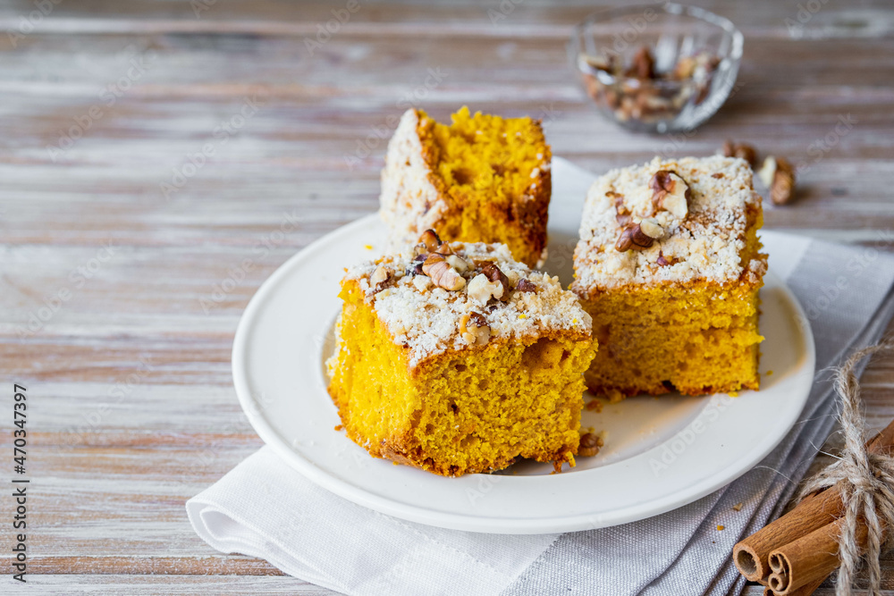 Wall mural Sliced pumpkin or carrot cake with streusel and walnuts on a white plate on a wooden background. Pumpkin baking recipes.