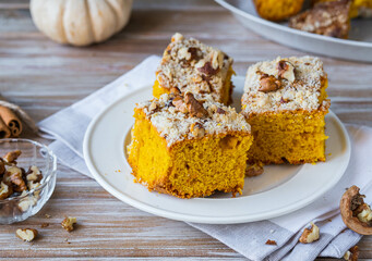 Sliced pumpkin or carrot cake with streusel and walnuts on a white plate on a wooden background. Pumpkin baking recipes.