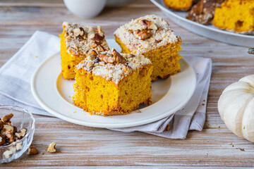 Sliced pumpkin or carrot cake with streusel and walnuts on a white plate on a wooden background....