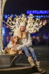 Fototapeta na wymiar a girl with a golden retriever dog on a winter night in a city decorated with lights