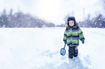 Fototapeta na wymiar A wonderful kid stands in a snowdrift with a shovel in his hands