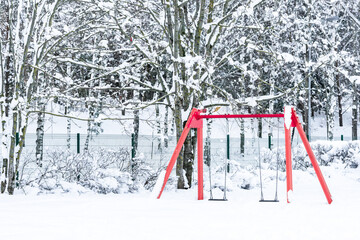 red swings at a snowed children playground