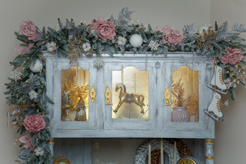 Beautiful shebby chic cupboard decorated with artificial snowy fir branches, icy roses, rocking horse toy, golden Christmas garland lights boke