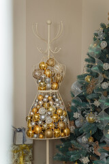 Mannequin or dummy full of golden shiny baubles, fir tree with white garlands on background. Merry Christmas, Happy new year