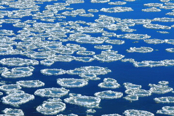 Frazil pancake ice in river with blue sky reflection