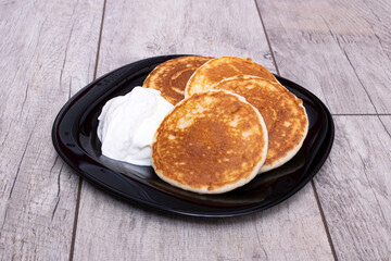 Pancakes and sour cream on plate on wooden table