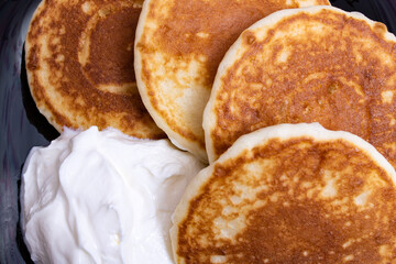 Pancakes and sour cream on plate on wooden table