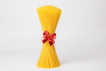 An upright bunch, a bunch of raw spaghetti tied with a rope with a red bow. Bundle on a white background. The concept of Italian food for the holiday.