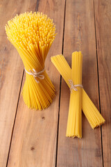 A vertical bunch and a bunch of raw spaghetti tied with string. Bundle on a wooden background....