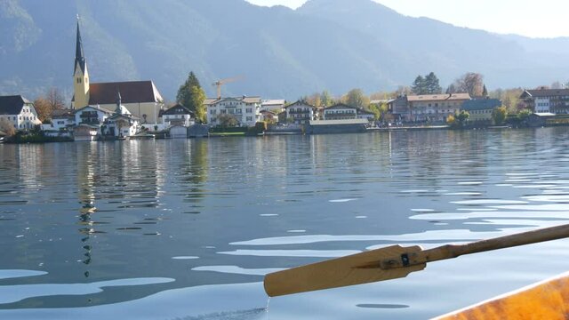A peaceful picture a wooden boat with an oar floats on beautiful mountain lake Tegernsee against backdrop of Alpine mountains and the picturesque container of the church. Ferryman ferries people
