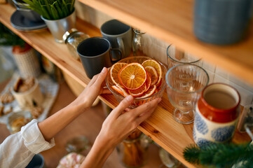 Merry Christmas and Happy New Year! Festive table setting and table decor for dinner. Women's hands take a plate with slices of dried orange from the kitchen shelf.