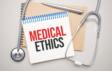 White notepad with the words medical ethics and a stethoscope on a blue background. Medical concept