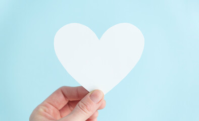 hand holding a white heart in blue background. Charity, pure love, compassion and kindness concept. Top view.