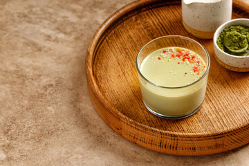 Matcha panna cotta dessert with confectionery decor in a glass on a wooden tray and beige background. Minimalistic and warm photography.