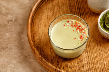 Matcha panna cotta dessert with confectionery decor in a glass on a wooden tray and beige background. Minimalistic and warm photography.