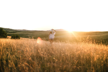 Woman walking through a field of tall grass at sunset