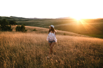 Naklejka na ściany i meble Woman walking through a field of tall grass at sunset