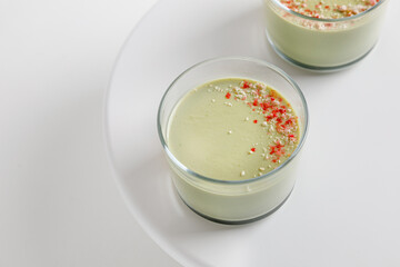 Matcha panna cotta desserts with confectionery decor in a glass on a white cake pan and white background.