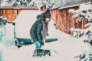 woman with shovel cleaning snow around car. Winter shoveling. Removing snow after blizzard