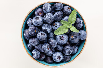 Ripe blueberries with water drops in a bowl on a pastel background,