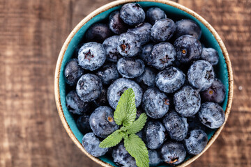 Ripe blueberries with water drops in a bowl on a wooden background,