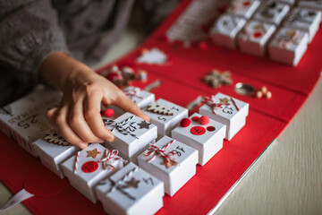 Obraz premium Pretty girl holds an original advent calendar made of jewelry boxes and a binder, New Year craft, diy. Magic of moment, seasonal activity. Christmas miracle. Soft focus, depth of field