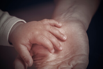 A woman's hand holding a newborn baby's hand